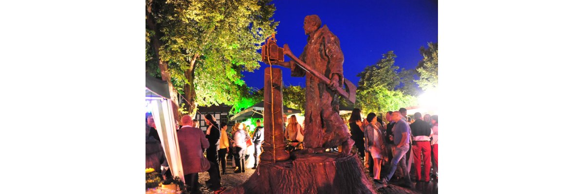 Bonifatius Skulptur mit Besuchern des Marktes im HIntergrund in Bund beleuchteter Atmosphäre