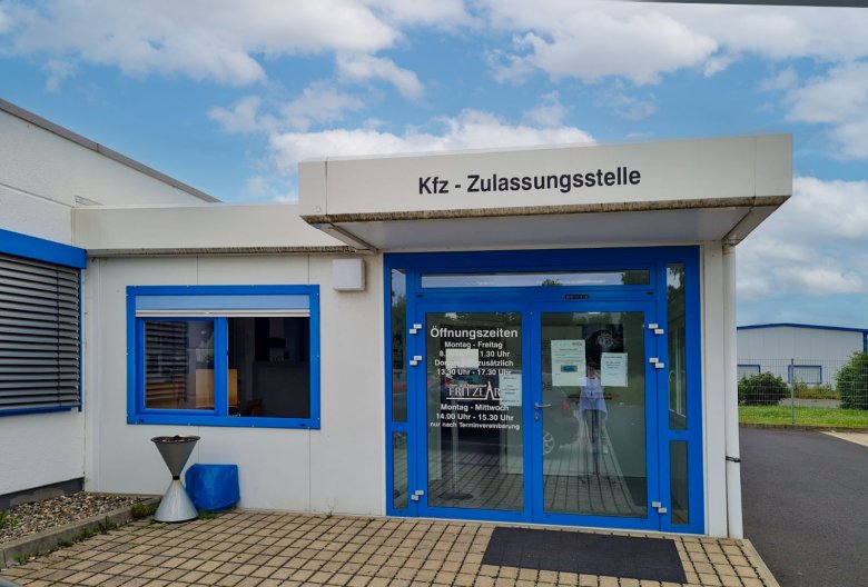 Eingangsbereich der Zulassungsstelle. Blauer Türrahmen mit Glasscheiben. Darüber eine Betonüberdachung mit der Aufschrift Kfz -Zulassungsstelle.