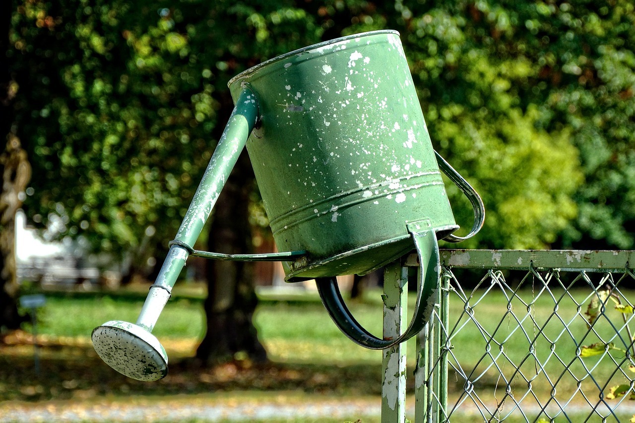 umgedrehte Gießkanne ohne Wasser auf Gartenzaun umgedrehte Gießkanne ohne Wasser auf Gartenzaun